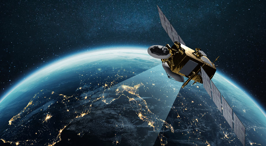 Satellite orbiting Earth at night, beaming a signal down toward illuminated city lights on the surface.